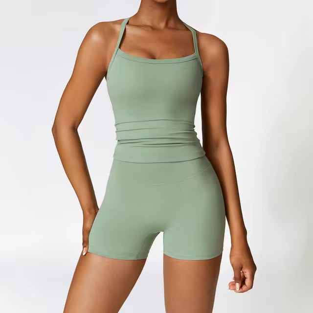 A woman posing in an olive green, two-piece workout set that includes shorts and a sleeveless shirt with straps