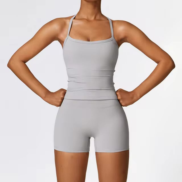 A woman posing in a grey, two-piece workout set that includes shorts and a sleeveless shirt