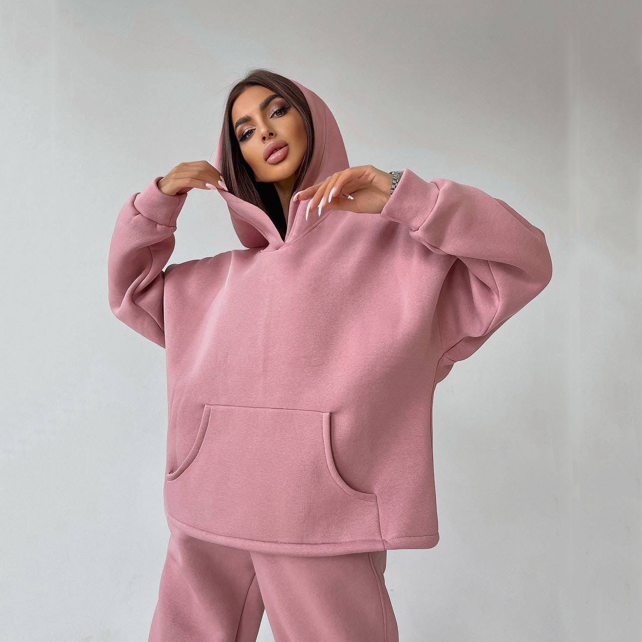 A woman posing in a pink, oversized hoodie with matching sweatpants