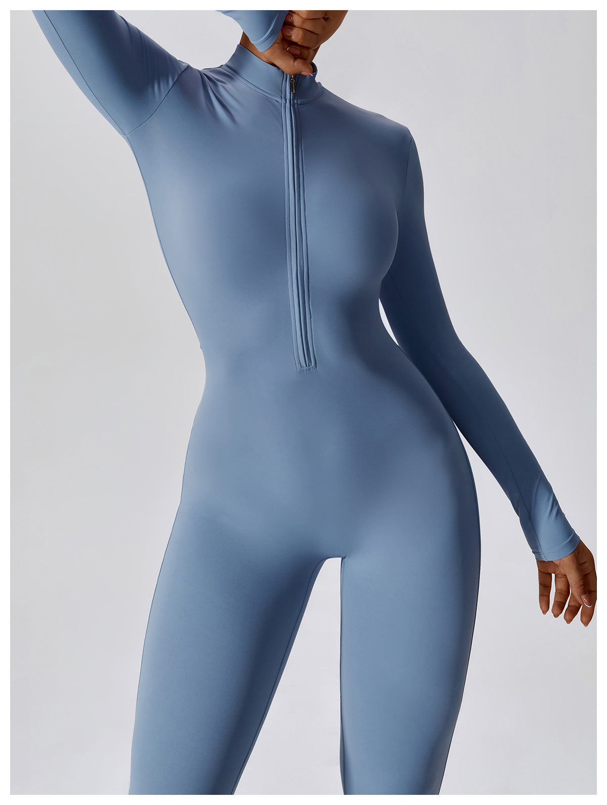 Woman posing in a long- sleeved, light blue, yoga jumpsuit with a zipper