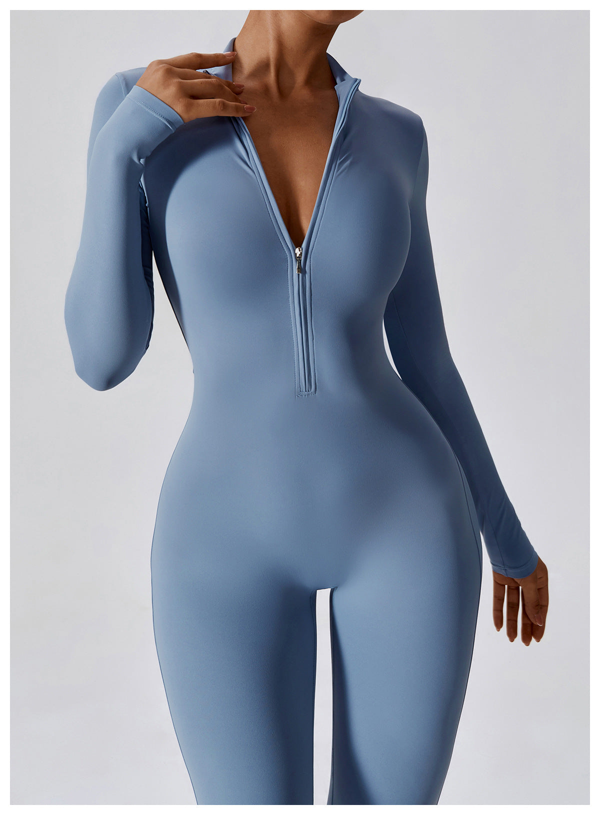 Woman posing in a long- sleeved, light blue, yoga jumpsuit with a zipper