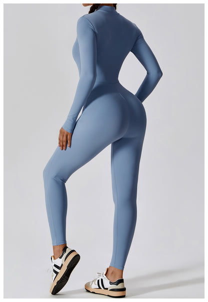 Woman posing in a long- sleeved, light blue, yoga jumpsuit with a zipper