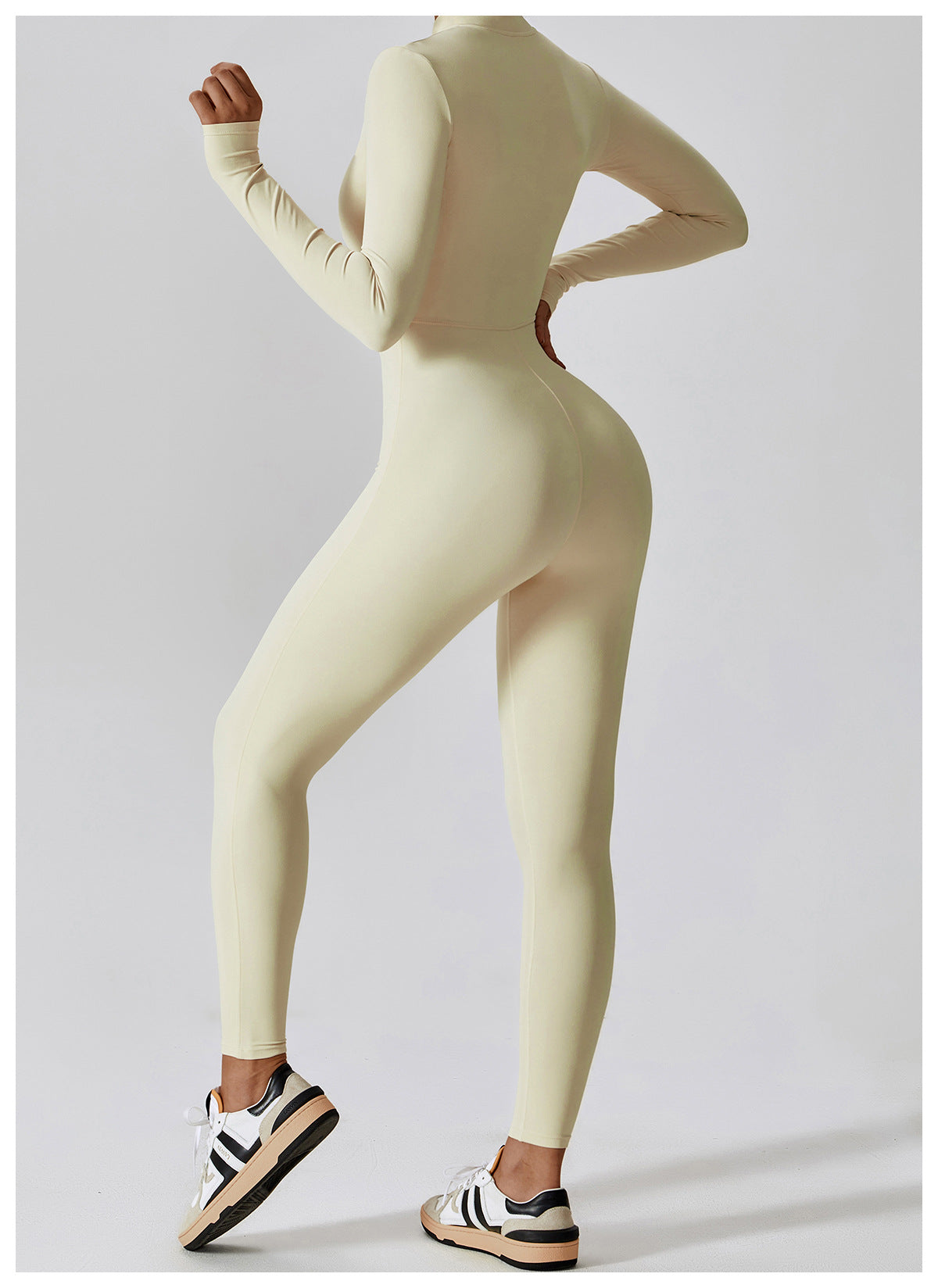 Woman posing in a long- sleeved, beige, yoga jumpsuit with a zipper