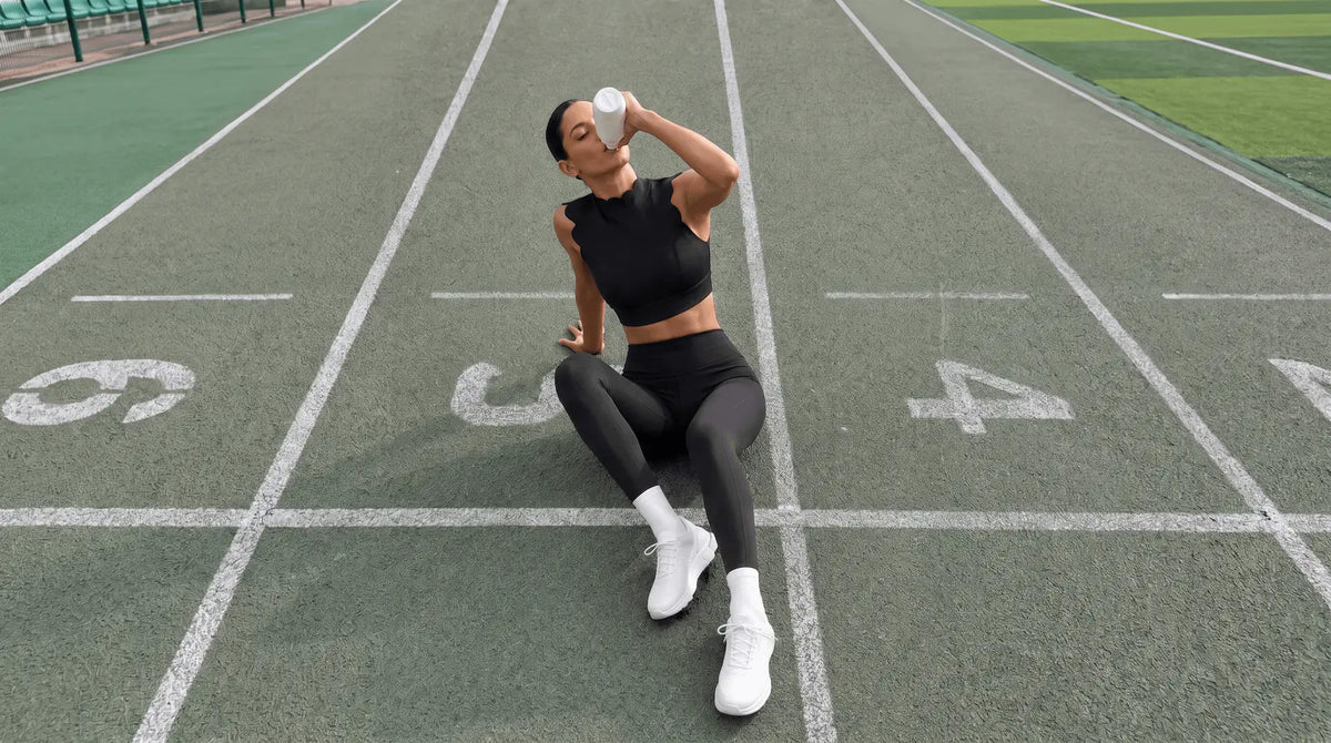 Seated on a running track in a black scallop-edge crop top and high-waist leggings
