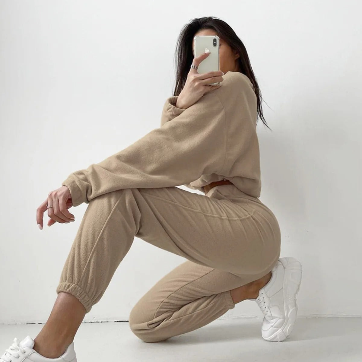 A woman posing in a beige matching set consisting of a sweatshirt and sweatpants