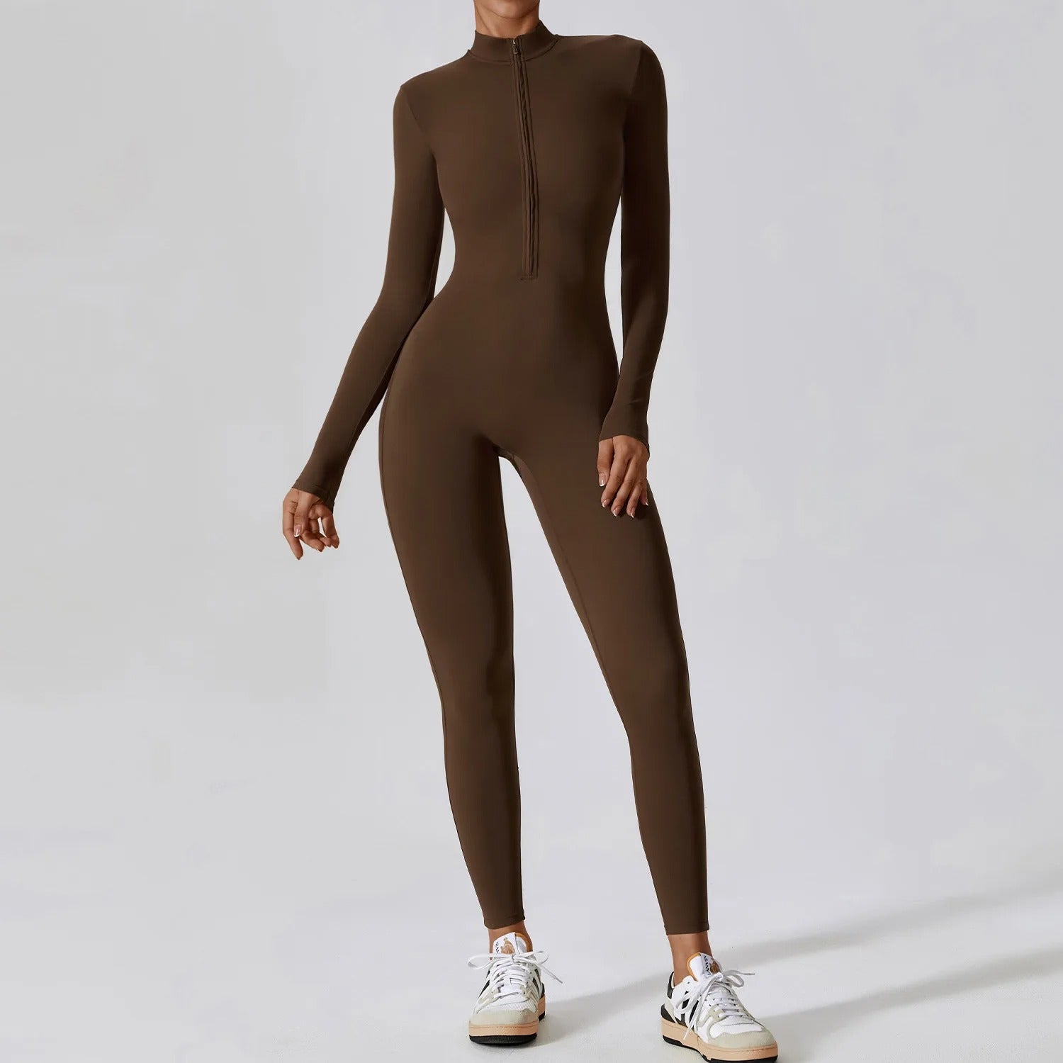 Woman posing in a long- sleeved, brown, yoga jumpsuit with a zipper