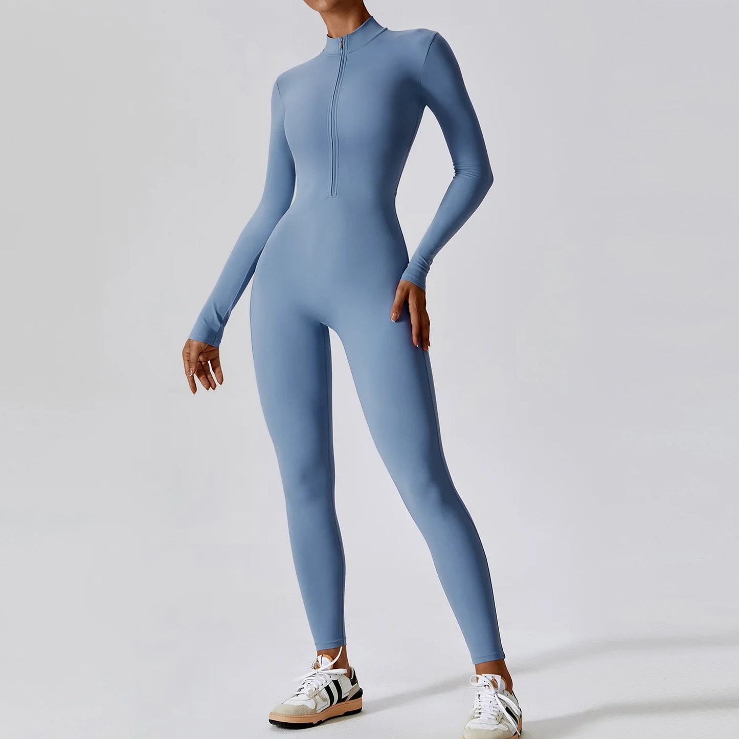 Woman posing in a long- sleeved, light blue, yoga jumpsuit with a zipper