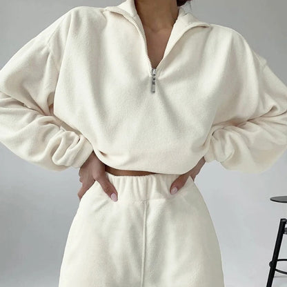 A woman posing in a white matching set consisting of a sweatshirt and sweatpants