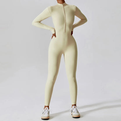 Woman posing in a long- sleeved, beige, yoga jumpsuit with a zipper