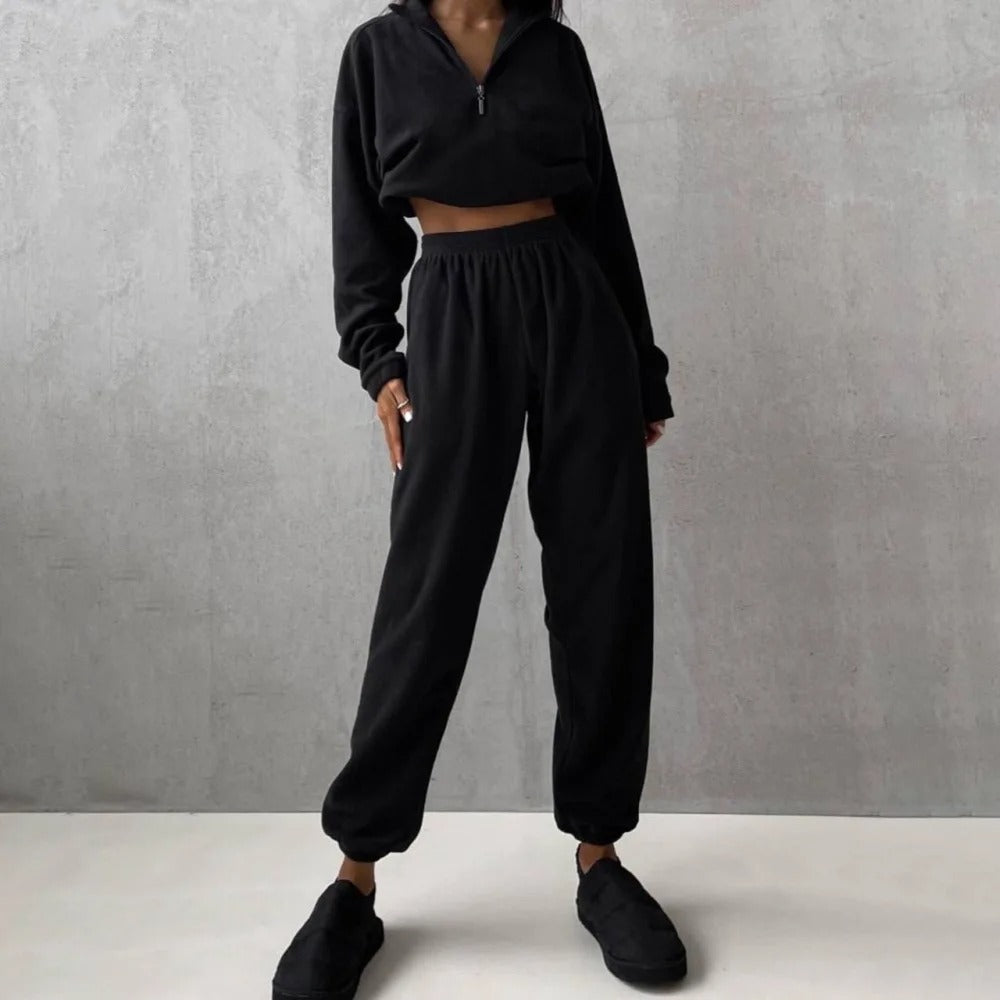 A woman posing in a black matching set consisting of a sweatshirt and sweatpants