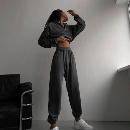 A woman posing in a black matching set consisting of a sweatshirt and sweatpants