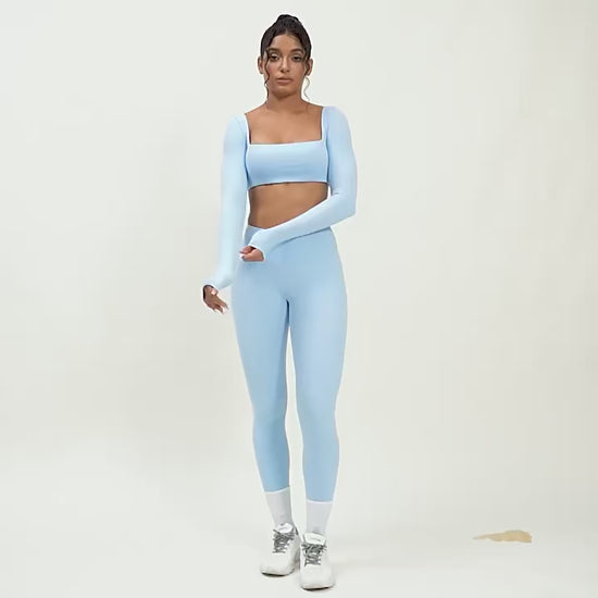 A woman posing in light blue leggings and a matching sports top