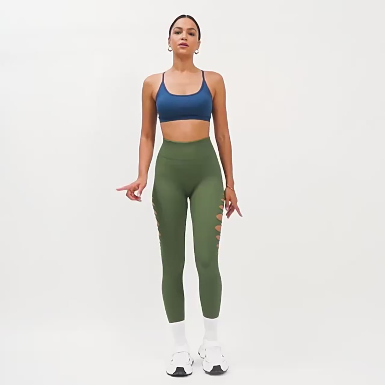 A woman posing in green yoga pants with holes on the sides and a blue gym top